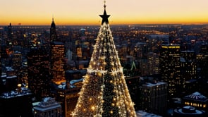 An AI-generated aerial view of a Christmas city at dusk, with glowing lights illuminating the Christmas tree and surrounding buildings.