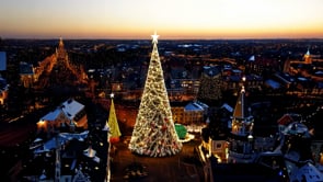 An enchanting aerial perspective of a city at sunset, featuring a glowing Christmas tree surrounded by holiday decorations and lights.