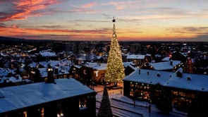 A charming aerial view of a village at sunset, with Christmas lights creating a soft glow over the rooftops, evoking a warm holiday feeling.