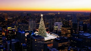 A breathtaking aerial view of a city at dusk, featuring a glowing Christmas tree surrounded by the soft glow of festive lights.