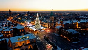 A picturesque aerial view of a city at sunset, showcasing holiday decorations and a brightly lit Christmas tree as the sun sets.