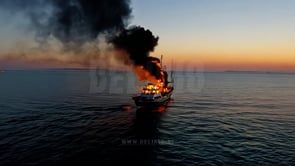 Fire consumes the ship as it drifts over calm sunset waves, with the scene exuding tension and beauty.