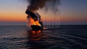 A ship set on fire drifts across the water during the twilight hours, with vibrant flames flickering in the dusk.