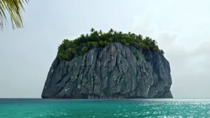 A scenic tropical beach shot featuring a rock island with palm trees in a dolly-in perspective.