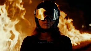 A burning inferno illuminates a motorbike, its fiery glow reflecting on a woman�s helmet visor, creating a dramatic image.