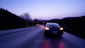 Defocused shot of a car's rear view at dusk, featuring blurry road lights under a soft evening sky.