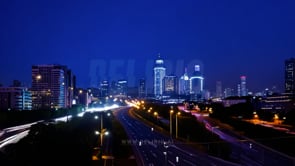 Wide-angle night time-lapse of cityscapes, showcasing traffic lights and towering buildings under a deep blue sky.