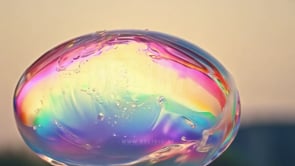 Soap bubble bursting in a close-up, revealing iridescent colors and textures tied to skincare and wellness.