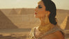 A woman from Ancient Egypt with artistic makeup, set against a blurred background of pyramids and desert, highlighting her beauty and cultural significance.