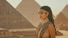 A headshot of a woman from Ancient Egypt captured in a dolly-in motion, with pyramids and desert blurred in the background, creating a dynamic and engaging portrait.