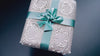 A white gift box with a green ribbon is seen from a top-down, close-up view, highlighting the box's detailed design.