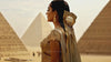 A woman from Ancient Egypt gazing directly at the camera, with a blurred background of pyramids and desert that adds depth to her striking presence.